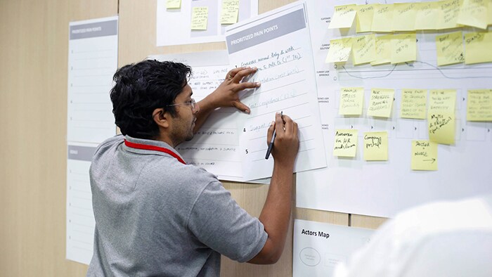 A man in a conference room leans against a wall while writing notes during a workshop